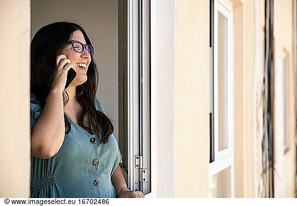Brunette spanish girl dressed on a business serius look talking on the phone at the window from her apartment during the afternoon in Palma de Mallorca  Spain during Coronavirus confinement