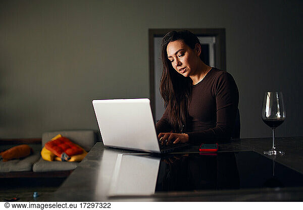 Brunette woman drinking wine and using laptop