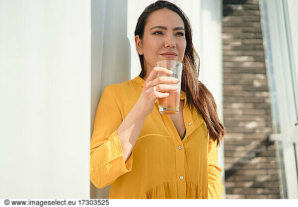 brunette woman drinks juice near the window