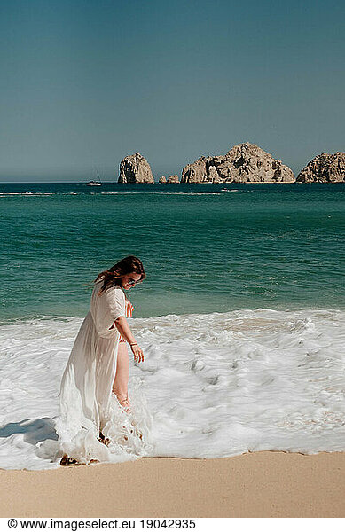 brunette woman in white cover-up in the waves of Cabo San Lucas