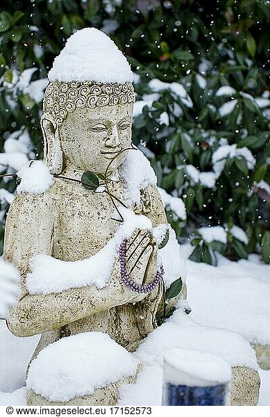 Buddha-Statue aus Stein unter dem Schnee in der Wintersaison in einem Garten.