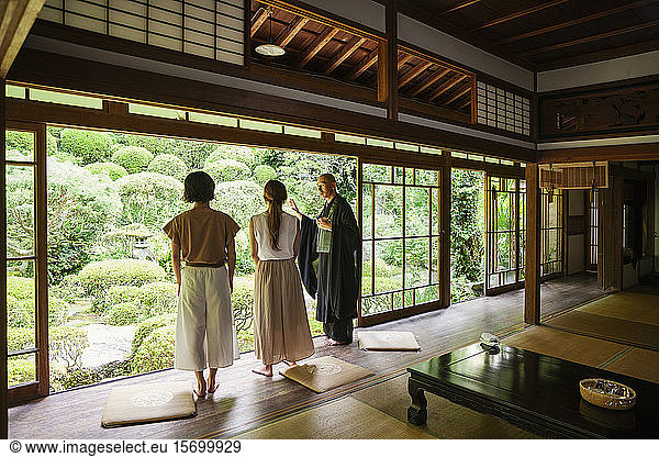 Buddhist priest and two Japanese women standing in Buddhist temple.