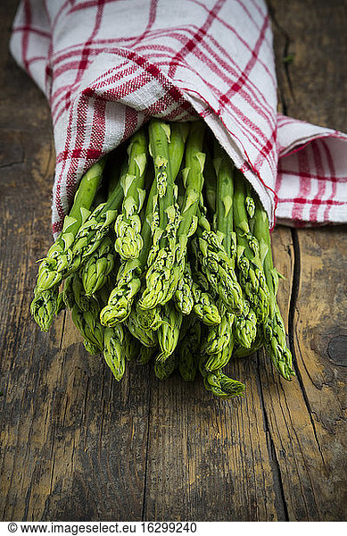Bunch of green asparagus  Asparagus officinalis  wrapped in kitchen towel lying on dark wood