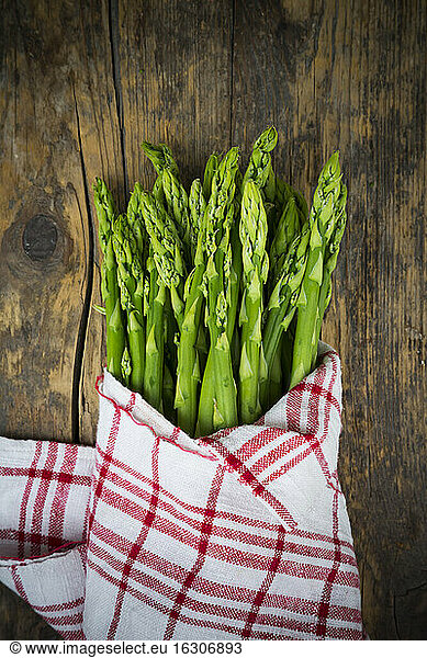 Bunch of green asparagus  Asparagus officinalis  wrapped in kitchen towel lying on dark wood