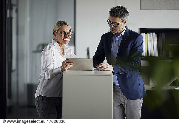 Business colleague discussing over tablet PC at desk in office