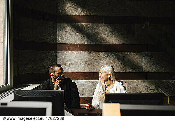Business colleagues discussing while sitting at desk during meeting in office