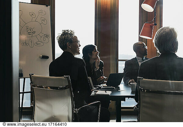 Business colleagues looking away while sitting at conference table planning strategy in board room during meeting at off