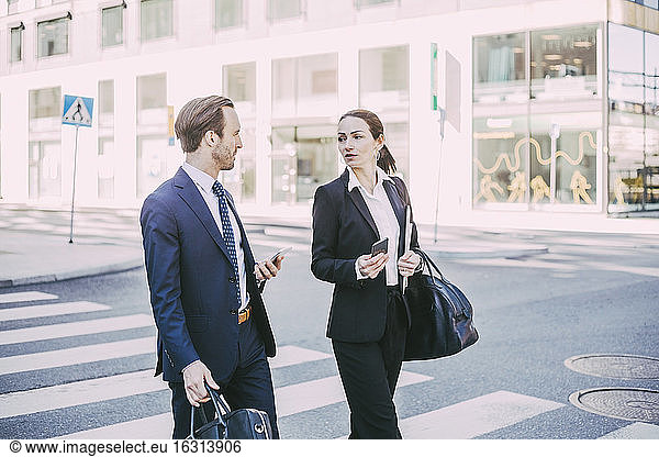 Business colleagues talking while crossing road in city