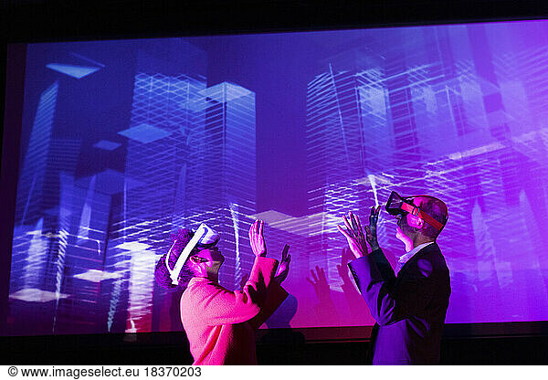 Business colleagues with futuristic glasses gesturing by projection screen at convention center