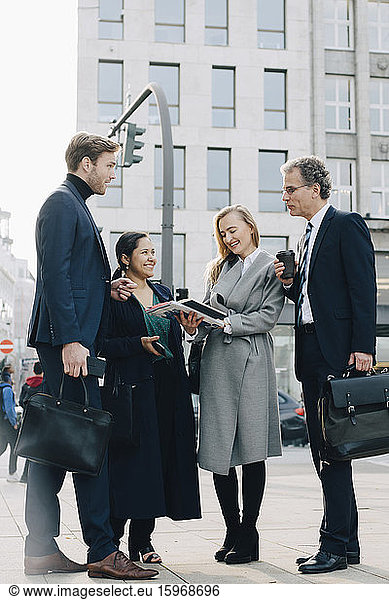 Business coworkers with book discussing while standing in city