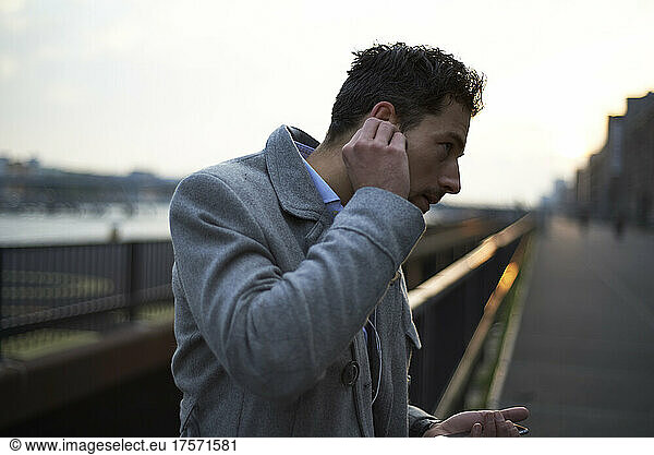 Business man at dawn in the city putting earbuds in his ear