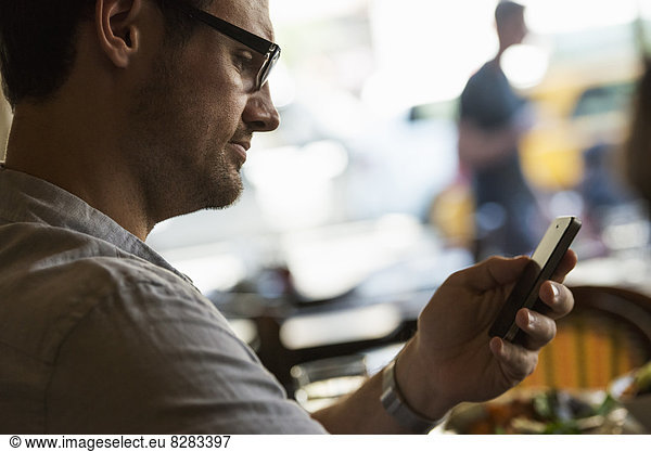 Business On The Go. A Man Sitting At A Cafe Table  Using His Mobile Phone. Looking Down At The Screen.