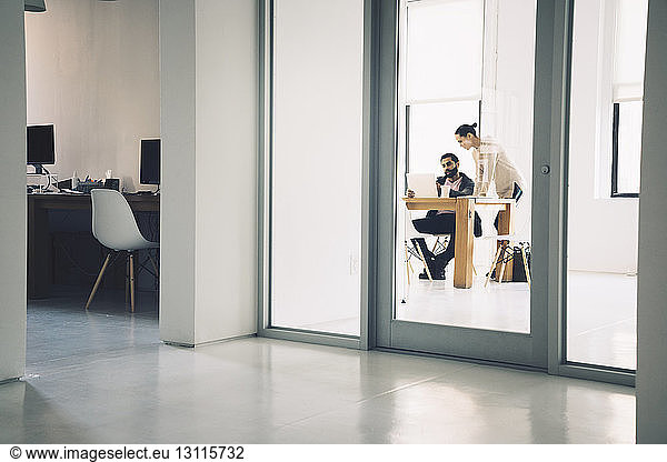 Business people discussing in office seen through doorway