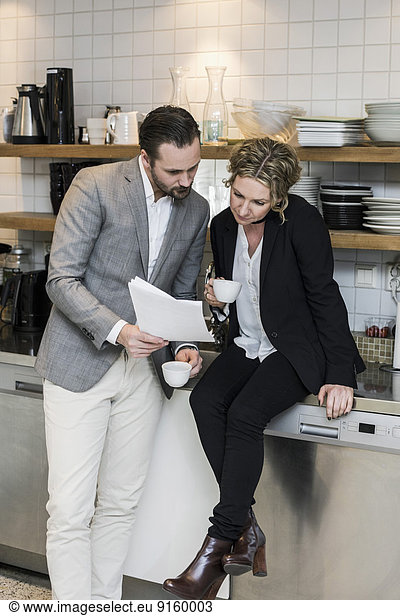 Business people having coffee while reading document at kitchen counter