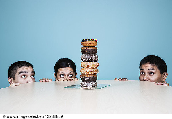 Business people hiding behind a table with a stack of doughnuts on it.