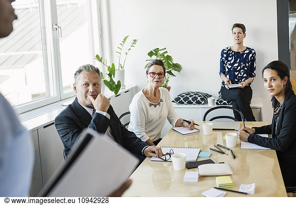 Business people looking at male colleague during meeting in office
