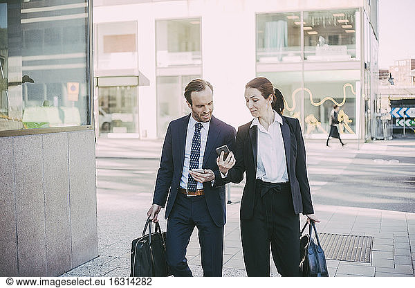 Business people talking while looking at smart phone in city