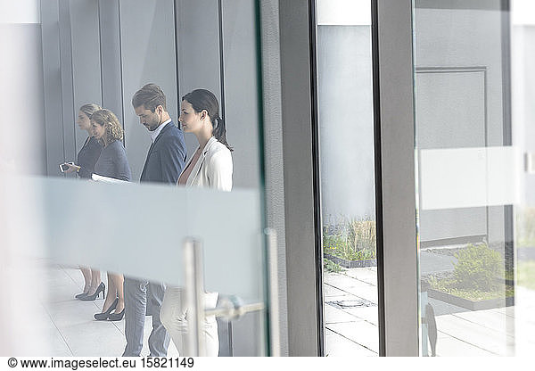Business people waiting in office building  leaning on glass pane