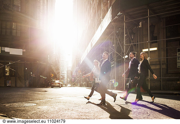 Business people walking on city street by buildings during sunny day