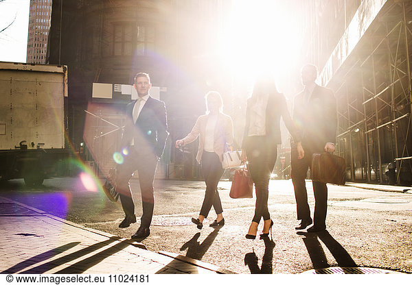 Business people walking on street against buildings during sunny day