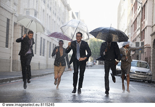 Business people with umbrellas running in rainy street