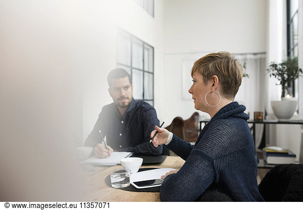 Business professional discussing with colleague during meeting at table