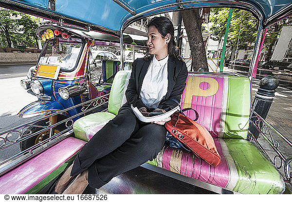business woman working on the backseat of a traditional Thai tuktuk