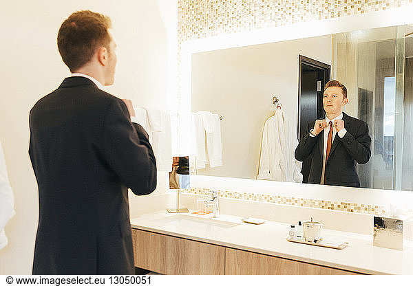 Businessman adjusting necktie in hotel bathroom