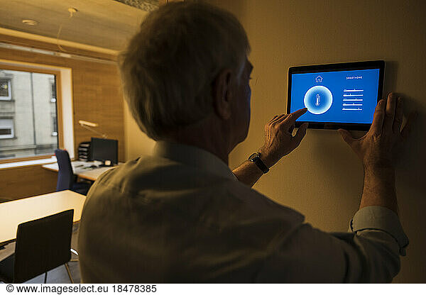 Businessman adjusting temperature through tablet PC mounted on wall at office