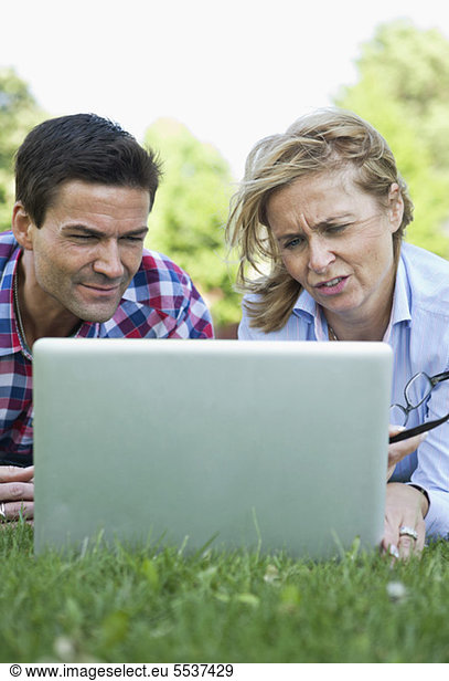 Businessman and business woman using laptop in grass