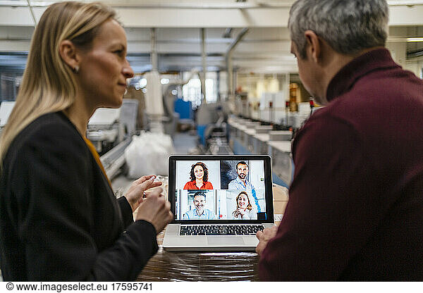 Businessman and businesswoman attending video call through laptop in factory