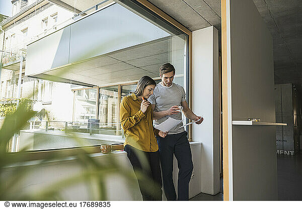 Businessman and businesswoman discussing documents at the window in office