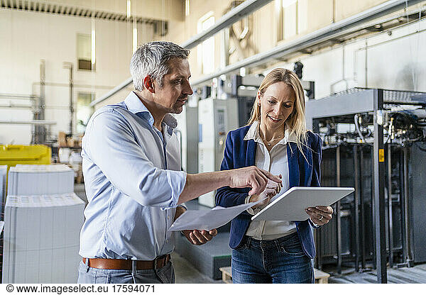 Businessman and businesswoman discussing over tablet PC in factory
