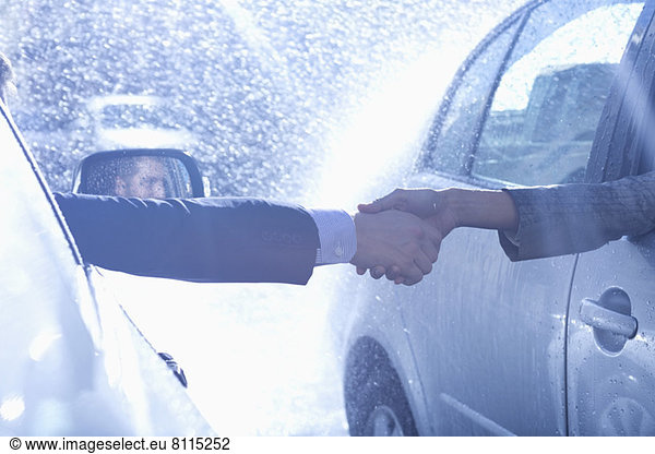 Businessman and businesswoman extending handshake from cars in rain