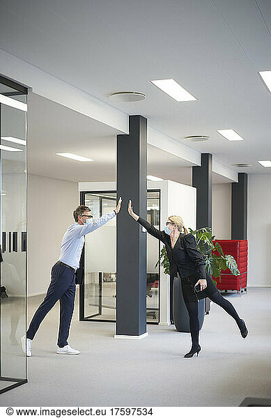 Businessman and businesswoman giving high-five and maintaining social distance in office