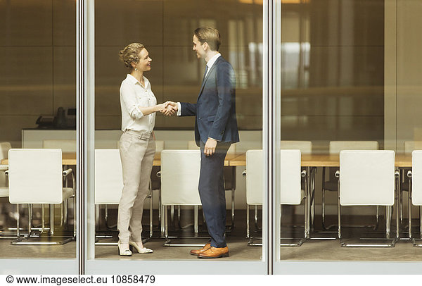 Businessman and businesswoman handshaking at conference room window