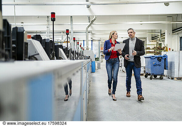Businessman and businesswoman sharing ideas walking in production wall