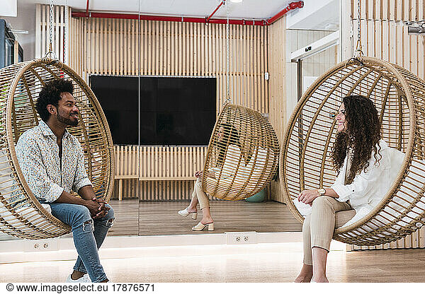 Businessman and businesswoman sitting in hanging chairs talking to each other