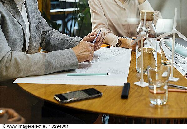 Businessman and businesswoman sitting with blueprints on table in office