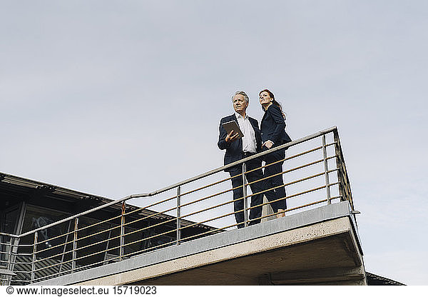Businessman and businesswoman standing on a balcony outside office building
