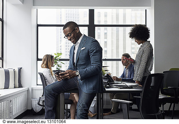 Businessman and businesswoman using smart phones while colleagues working in office