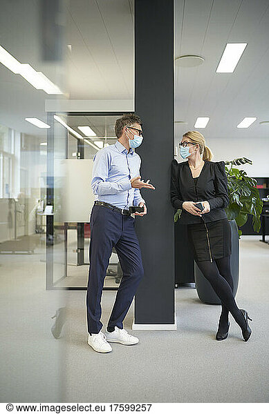 Businessman and businesswoman wearing protective face masks and talking in office