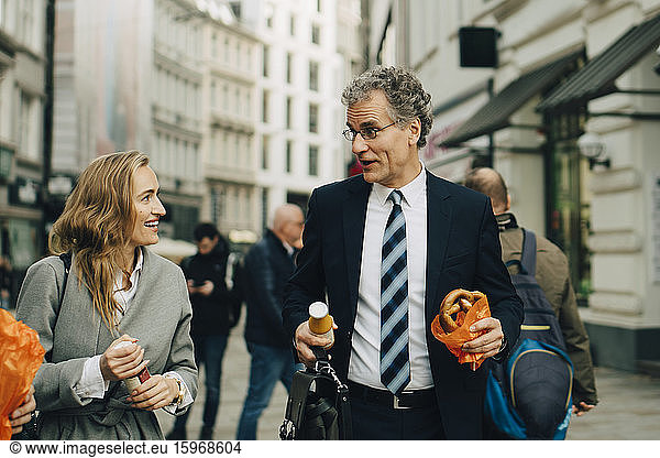 Businessman and businesswoman with meal walking in city