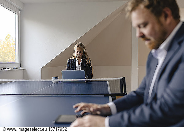 Businessman and businesswoman working at table tennis table in office
