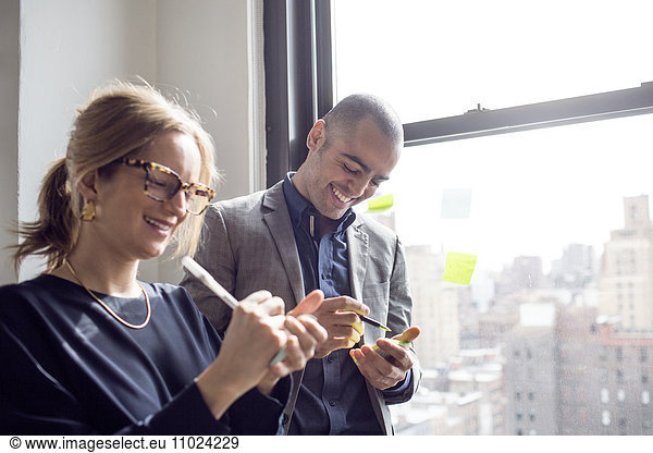 Businessman and businesswoman writing on sticky notes by window