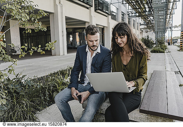 Businessman and casual businesswoman using laptop outdoors