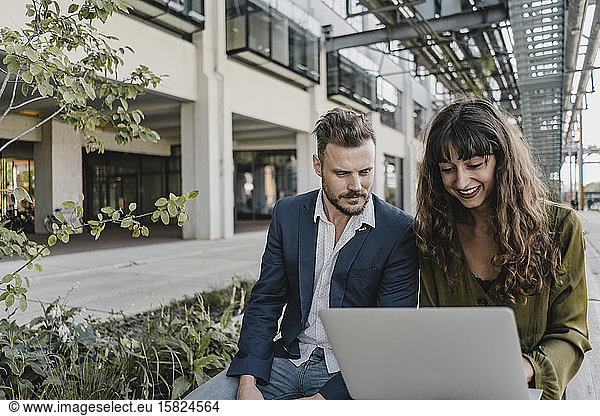Businessman and casual businesswoman using laptop outdoors