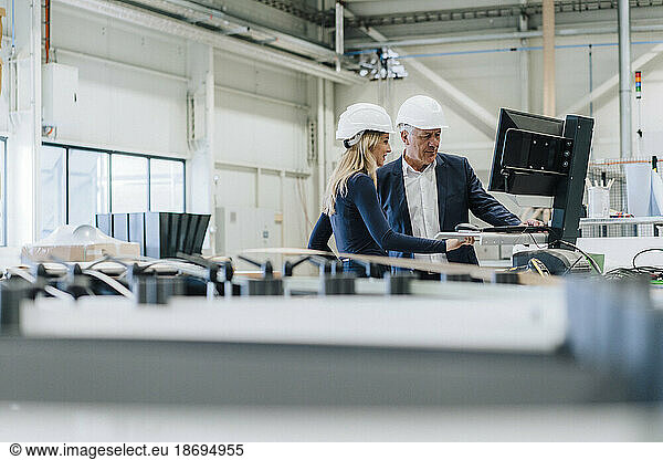 Businessman and colleague working on desktop PC in factory