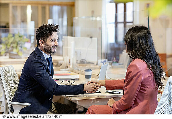 Businessman and female entrepreneur handshaking at coworking office