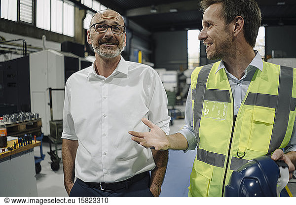 Businessman and man in reflective vest talking in a factory
